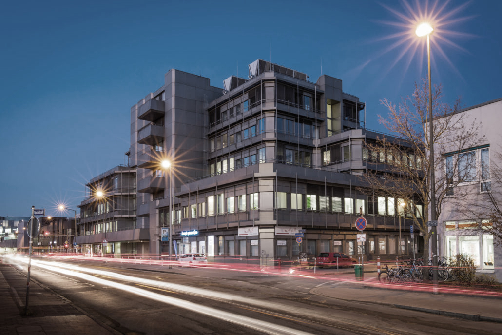 Moderne Bürogebäude bei Nacht mit städtischer Beleuchtung und Verkehr in der Innenstadt.