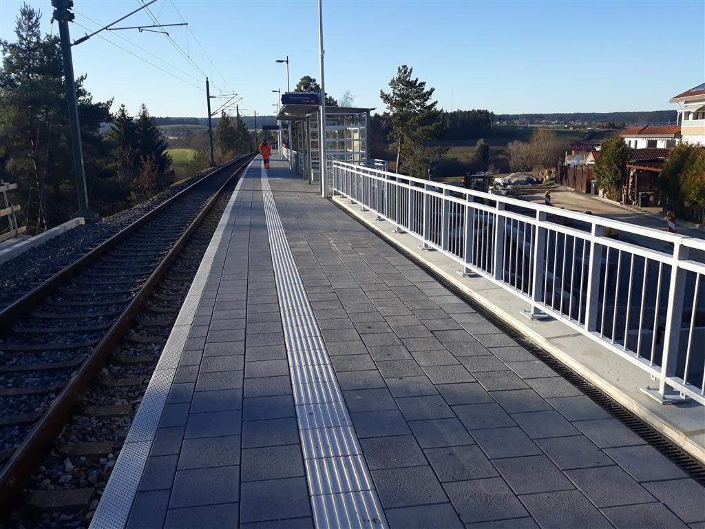Schmaler Bahnsteig mit barrierefreier Zugangsrampe an der Bahnlinie.