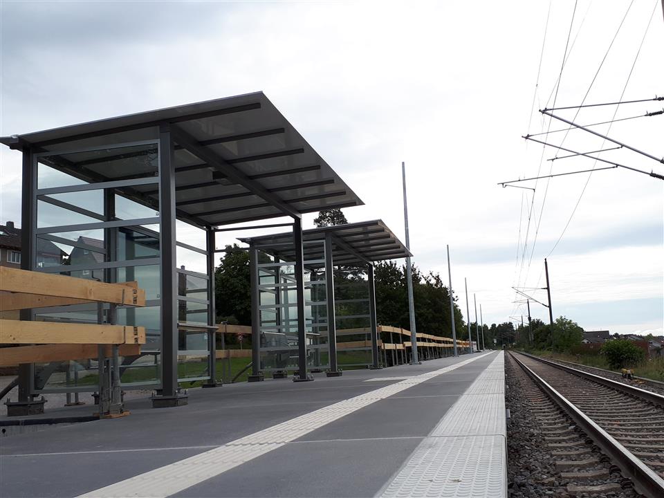 Praktischer, moderner Bushaltestellenbau am Bahnhof mit Wartebereich und Zuggleis.