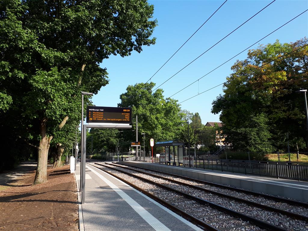 1. Bahnsteig mitfahrendes Zugabfahrtanzeigetafel und grünen Bäumen bei schönem Wetter.