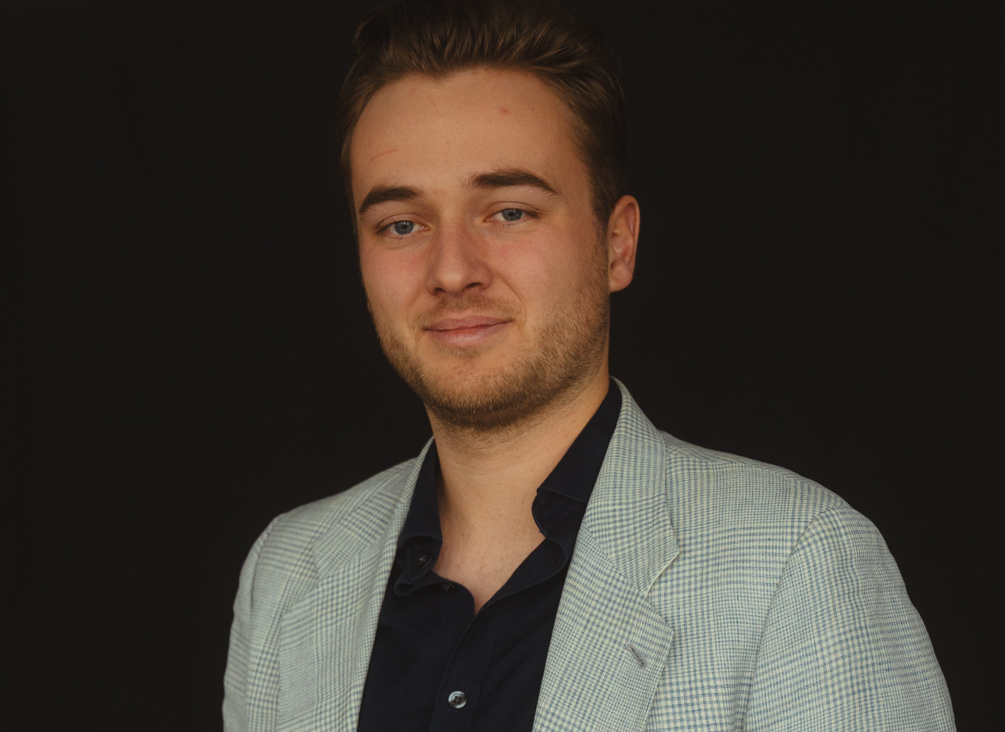 Hochwertiges Business-Porträt eines jungen Mannes in Anzug vor schwarzem Hintergrund.